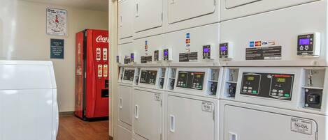 A laundry room with multiple washing machines, a Coca-Cola refrigerator, and payment card machines.