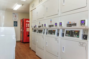 Uma lavanderia com várias máquinas de lavar, um refrigerador Coca-Cola e máquinas de cartão de pagamento.