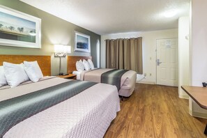 A hotel room with two beds, a nightstand, a lamp, a painting, and a door.
