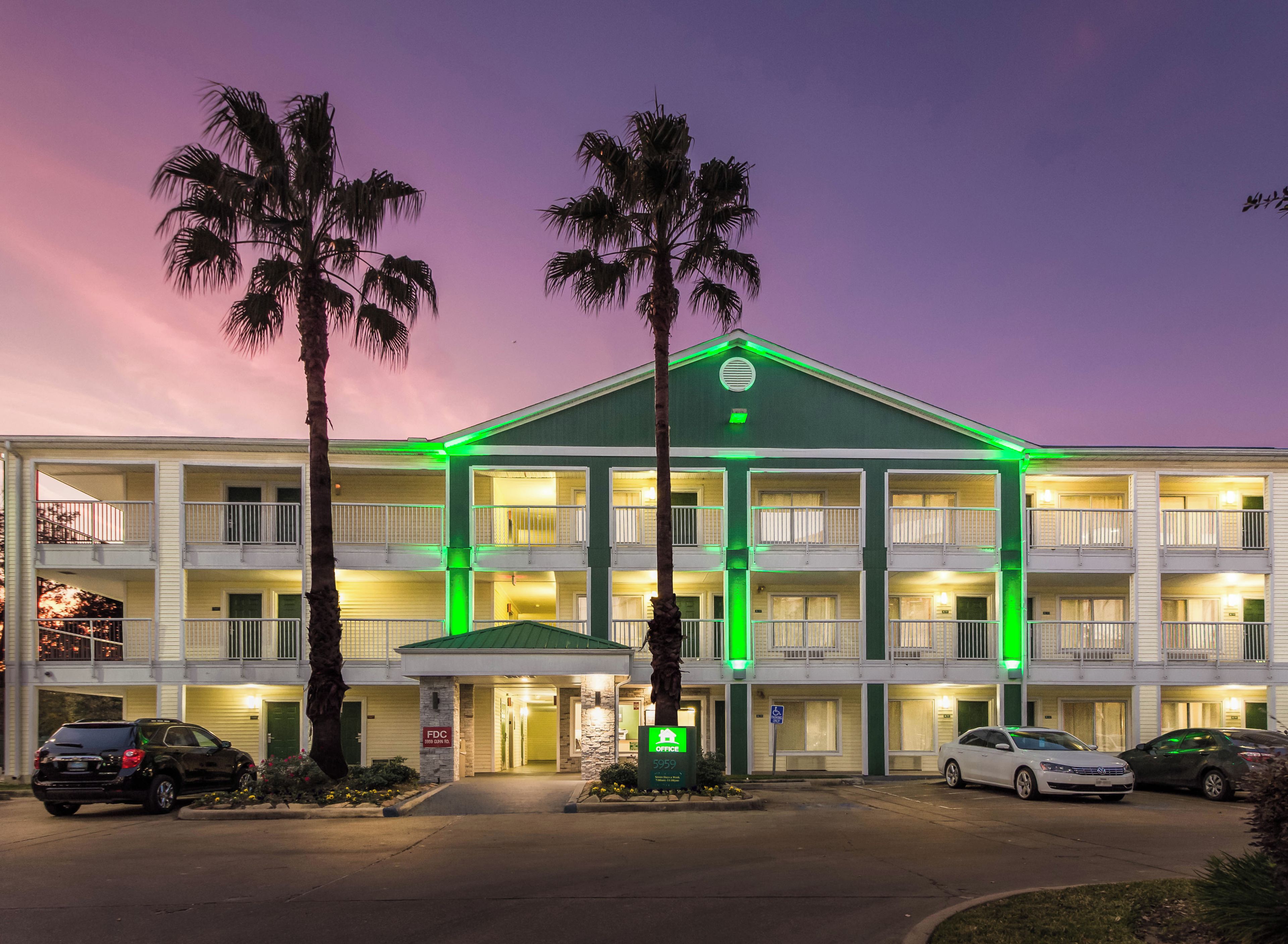 A multi-story hotel with a green roof, multiple balconies, and a parking area with cars.