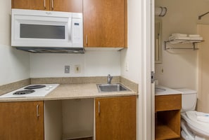 Una cocina compacta con microondas, estufa, fregadero y armarios de madera.
