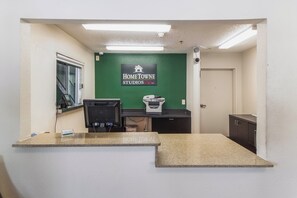 Zona de recepción con pared verde, mostrador de recepción, impresora y cámara de seguridad.