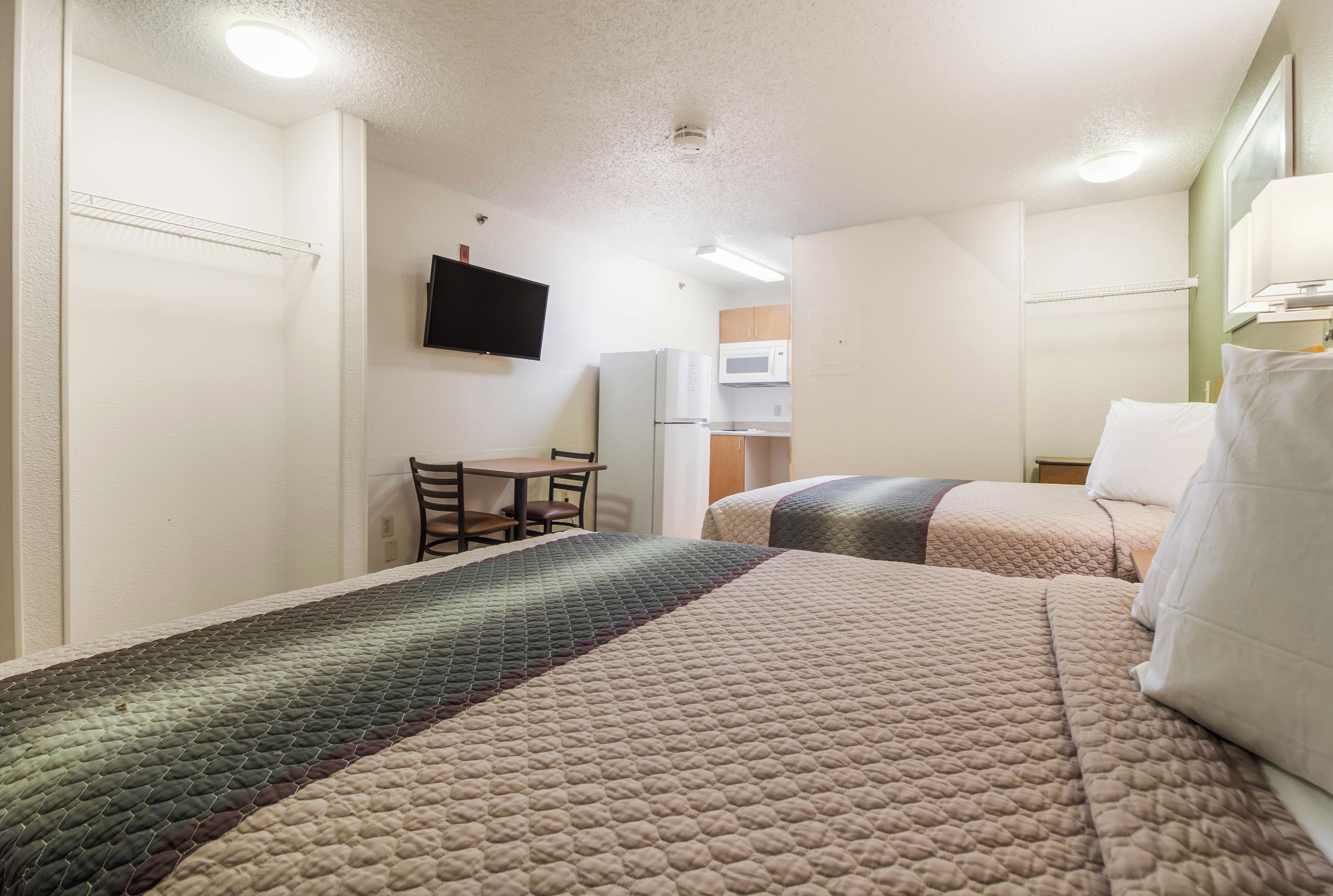 A hotel room with two beds, a desk, a television, and a microwave.