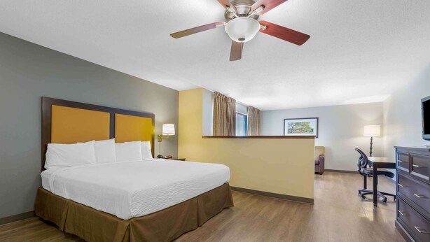 Quarto de hotel com uma cama grande, uma escrivaninha, uma cadeira, um ventilador de teto e uma televisão.