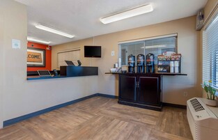 Zona de recepción con mostrador, televisor y estación de café con varios dispensadores.