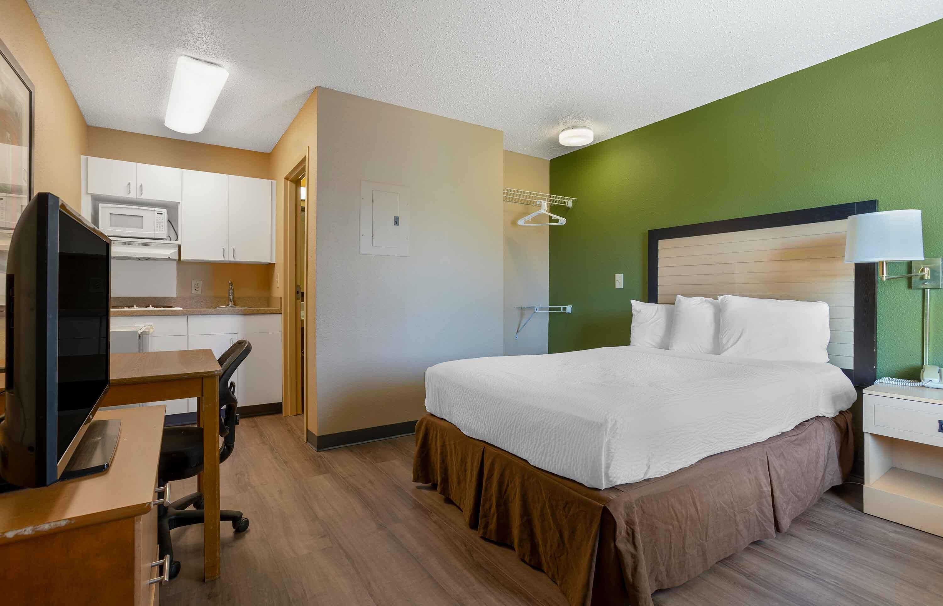 Une chambre d’hôtel équipée d’un lit, d’un bureau, d’une chaise, d’une télévision, d’un four à micro-ondes et d’un mur d’accent de couleur verte.