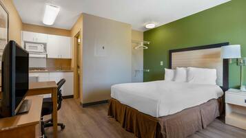 Une chambre d’hôtel équipée d’un lit, d’un bureau, d’une chaise, d’une télévision, d’un four à micro-ondes et d’un mur d’accent de couleur verte.