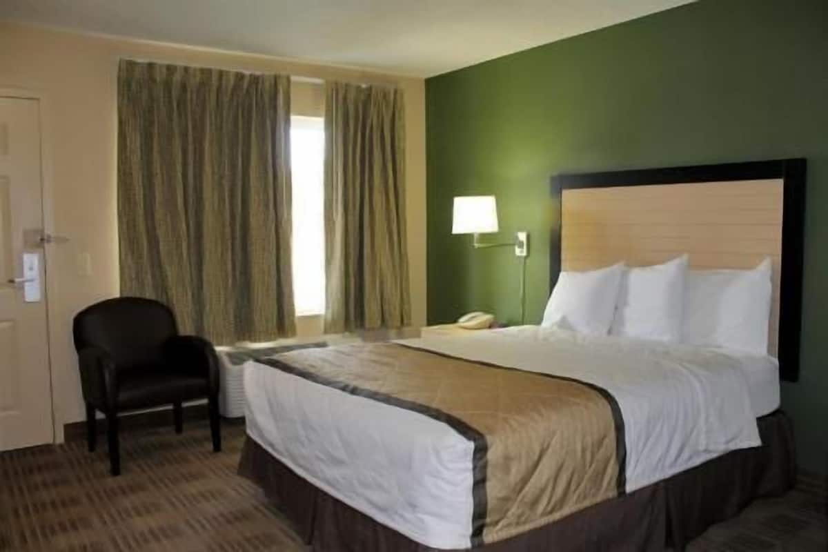 A hotel room with a bed, a chair, a lamp, and curtains.