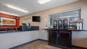 A reception area with a 'WELCOME' sign, a reception desk, a television, and a coffee station with multiple dispensers. - Extended Stay America Suites Houston The Woodlands (Spring)
