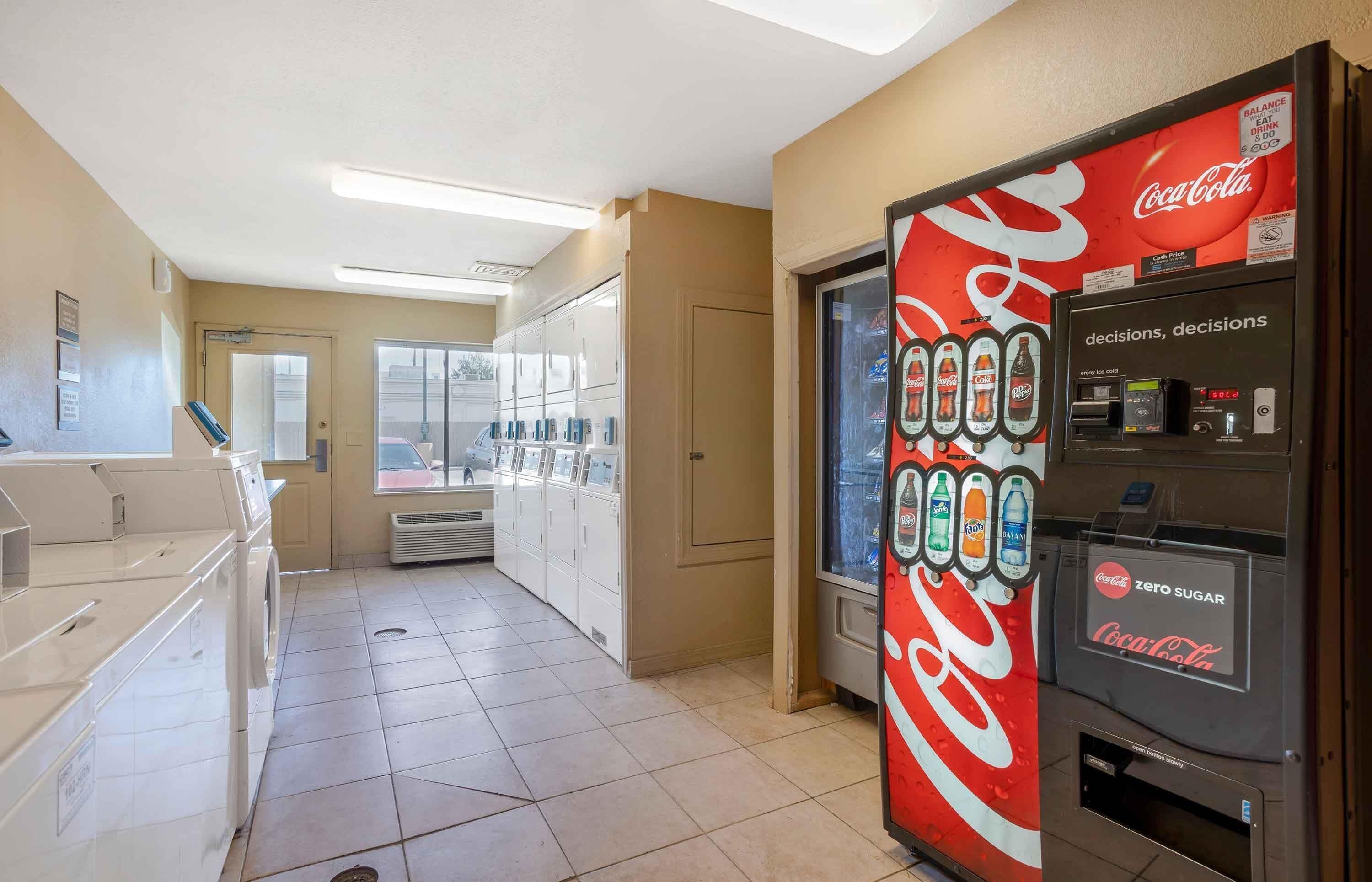 A hotel corridor with a vending machine on the right, a laundry area on the left, and a view of the outside.