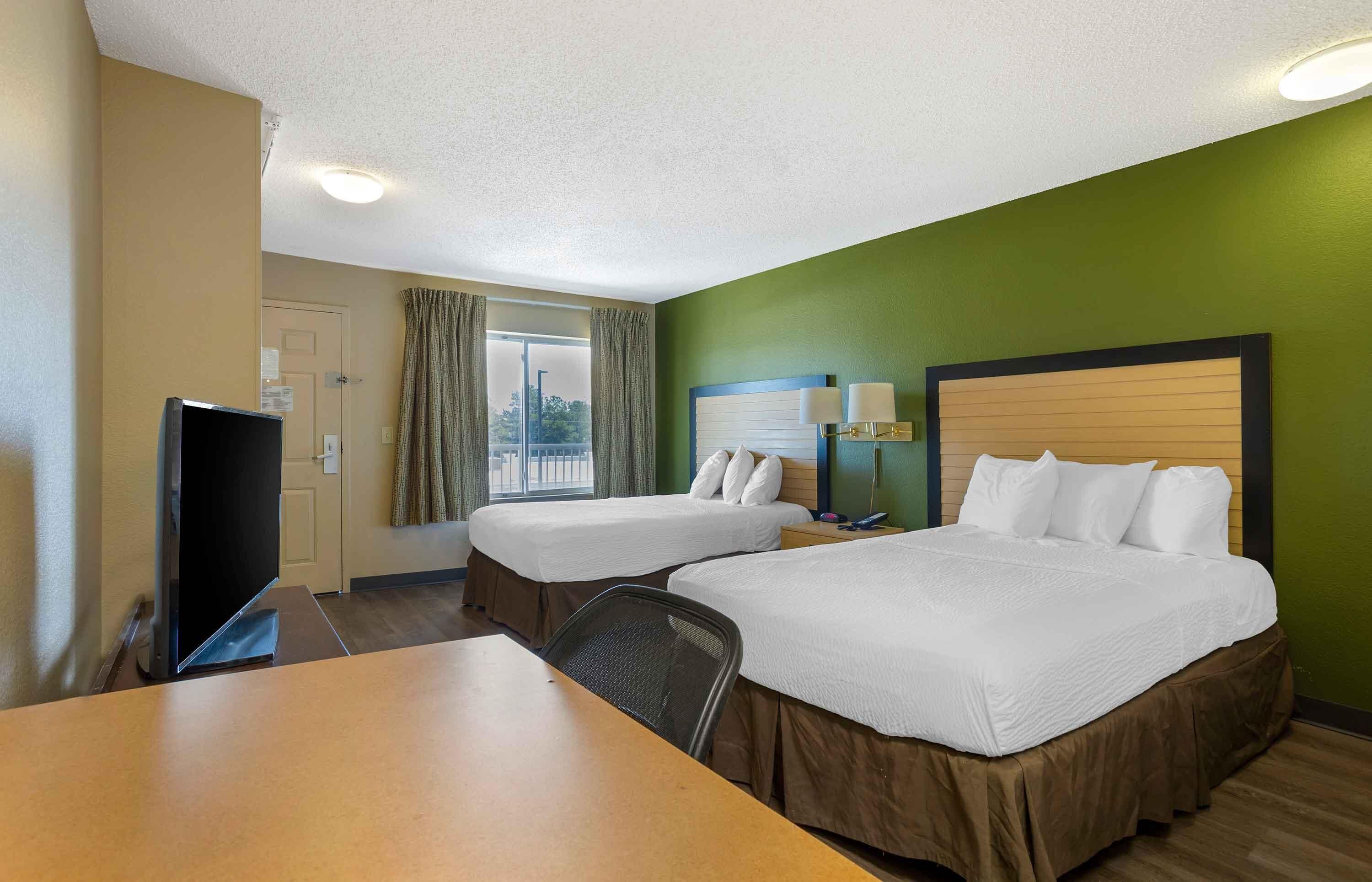 Habitación de hotel con dos camas, un escritorio, televisión y ventana con cortinas.