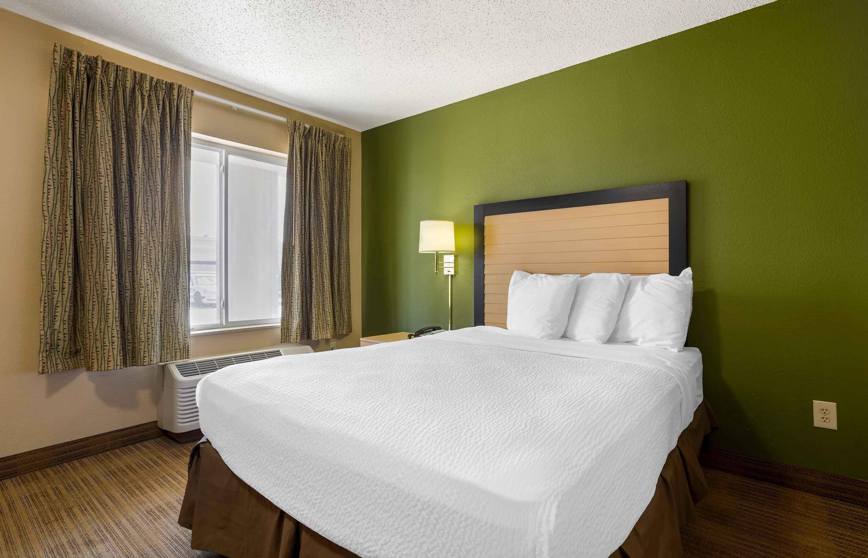 A hotel room with a large bed, a bedside lamp, and a window with curtains.