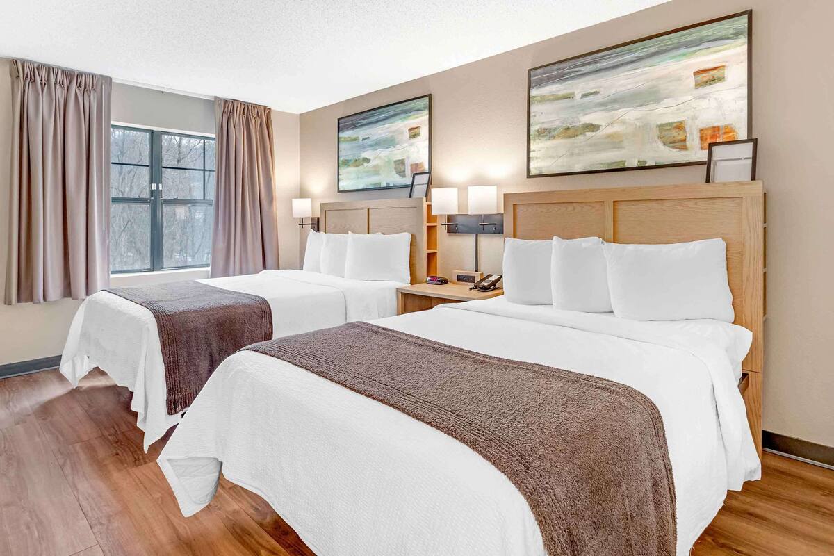 Une chambre d’hôtel avec deux lits, une grande fenêtre avec des rideaux et des tableaux abstraits accrochés au mur.