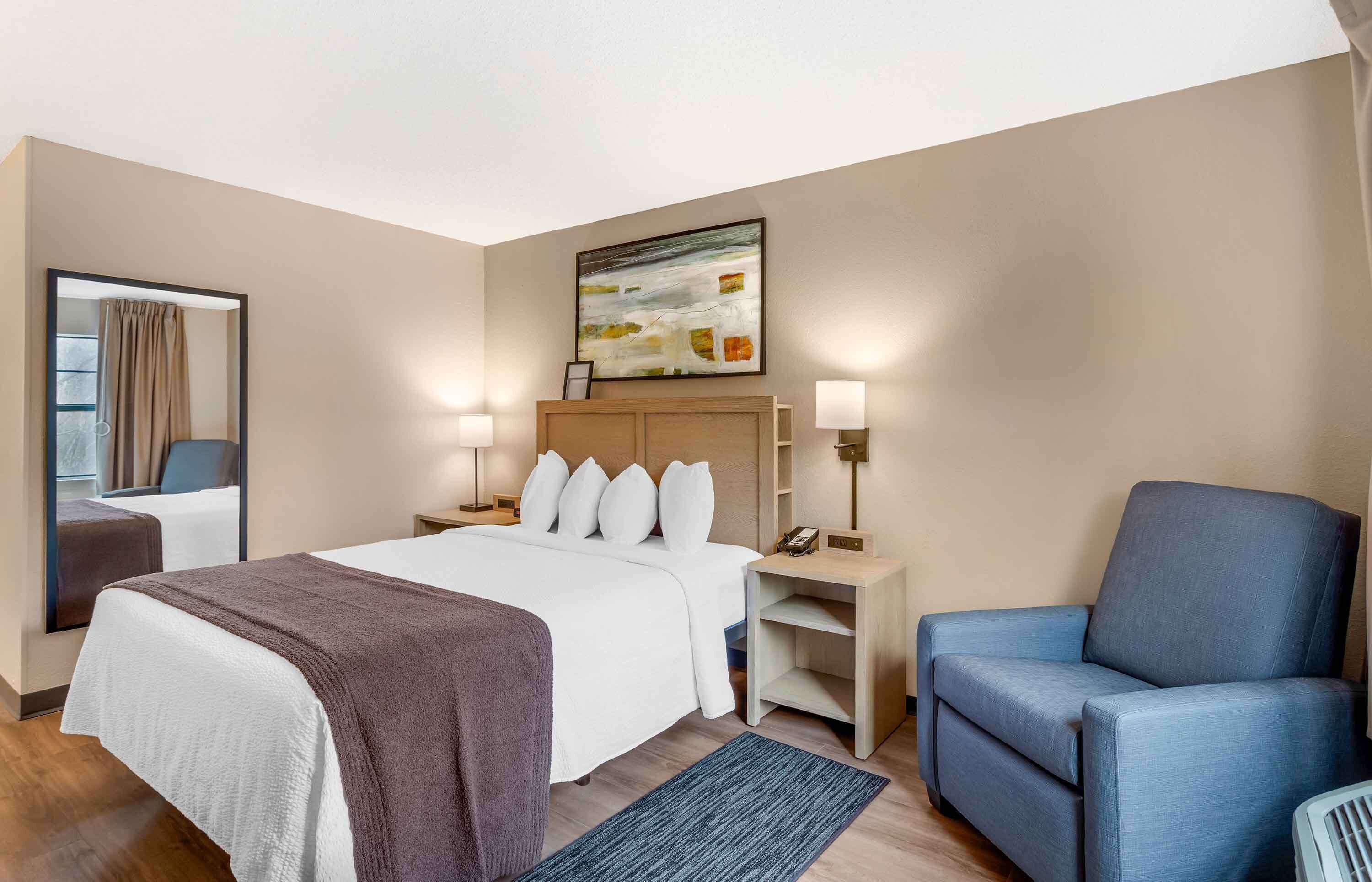 Une chambre d’hôtel avec un grand lit, deux tables de chevet avec des lampes, un fauteuil bleu et un tableau au mur.