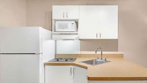 A compact kitchen with white cabinets, a built-in microwave, a stove, and a sink. - Extended Stay America Suites Asheville Tunnel Rd (Asheville)