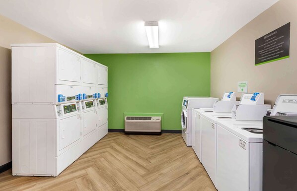 A laundry room with multiple washing machines and dryers, a ventilation unit, and a sign on the wall. - Extended Stay America Suites Asheville Tunnel Rd (Asheville)