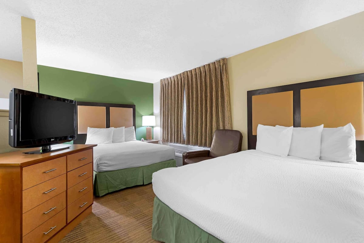 A hotel room with two beds, a TV, a desk, and a chair.