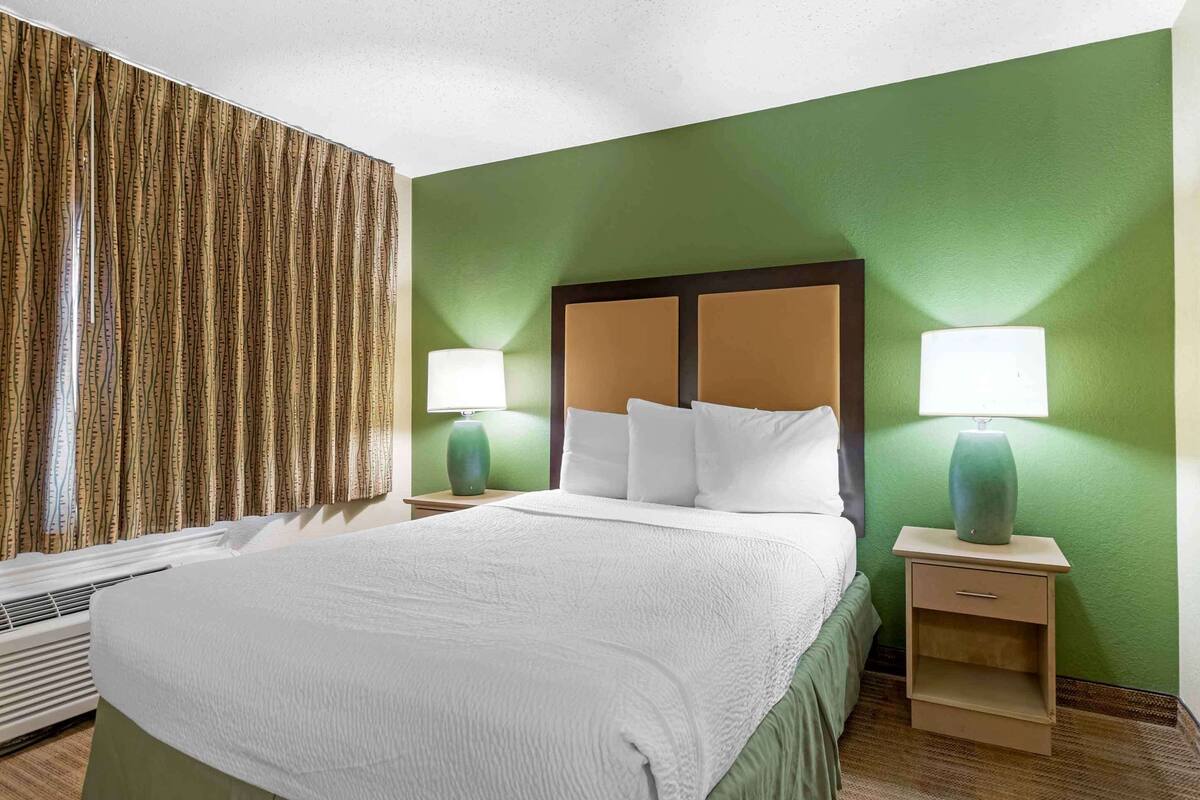 A hotel room with a large bed, two bedside tables with lamps, a green wall, and a window with curtains.