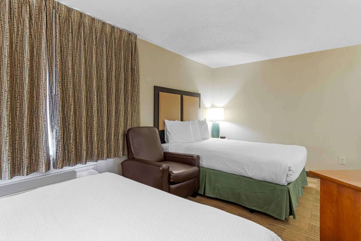 A hotel room with two beds, a brown leather chair, a nightstand, and a lamp.
