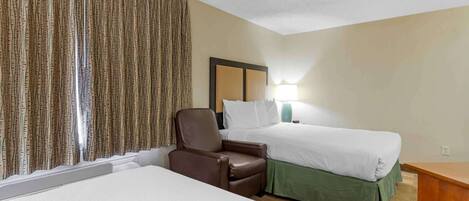 Quarto de hotel com duas camas, uma poltrona de couro marrom, uma mesa de cabeceira e um abajur.