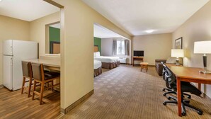 Ein Hotelzimmer mit Küchenzeile, Essbereich, Bett, Fernseher und Schreibtisch mit Lampe.