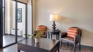 Ein Hotelzimmer mit einem großen Fenster, einem Schreibtisch mit einer Pflanze, zwei Stühlen mit gemusterten Kissen, einer Lampe und einem kleinen Tisch.