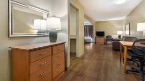 A hotel room with a wooden dresser, a desk with a chair, a television, and a large mirror. - Suburban Studios Macon North (Macon)