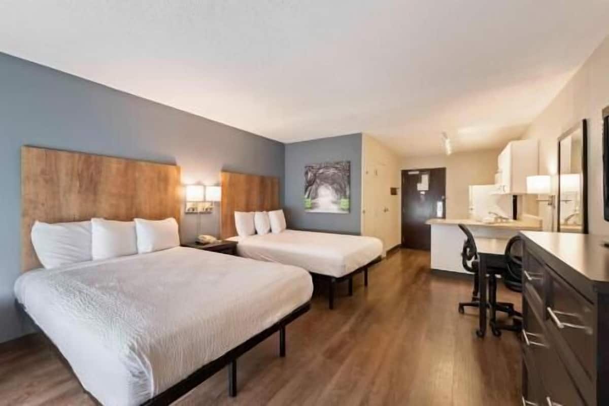 A hotel room with two beds, a desk, a chair, and a painting on the wall.