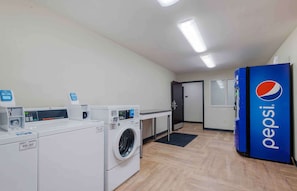 A laundry facility with multiple washing machines, a drying area, and a Pepsi refrigerator.