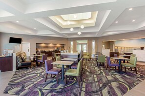 A hotel lobby with a modern design, featuring a central seating area with tables and chairs, a kitchen area, and a reception desk. - La Quinta Inn & Suites by Wyndham Panama City (Panama City)