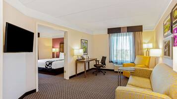 A hotel room with a bed, a desk with a chair, a sofa, a TV, and a window with curtains.