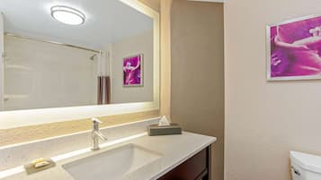 A bathroom with a large mirror, a sink, a toilet, and a framed artwork on the wall.