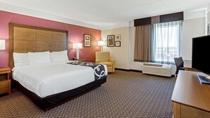 Ein Hotelzimmer mit einem großen Bett, einem Schreibtisch, einem Stuhl, einem Fernseher und einem Fenster mit Vorhängen.