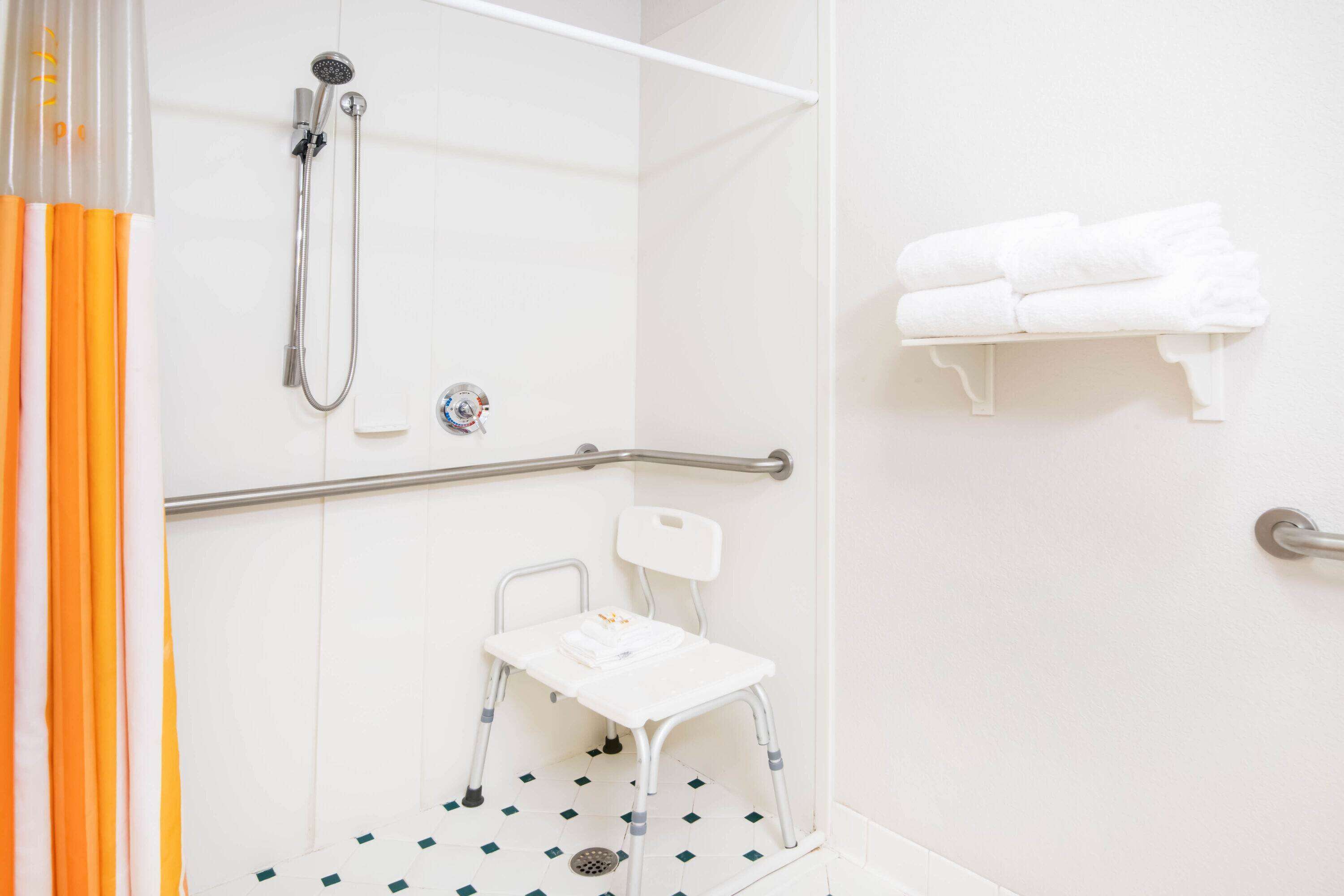 A shower area with a grab bar, a white chair, and a towel rack.