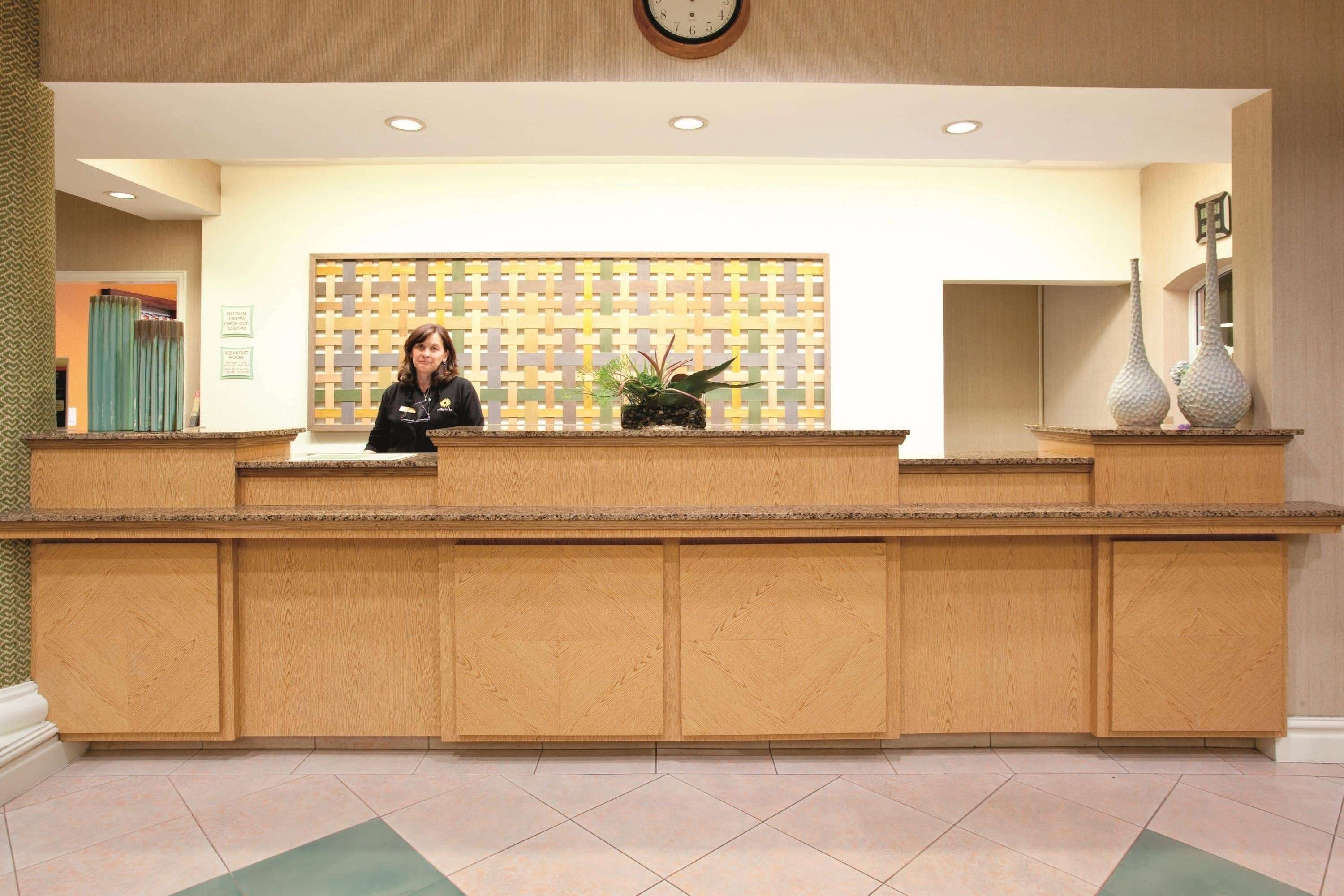 A reception desk with a receptionist, a patterned wall, and a clock above.