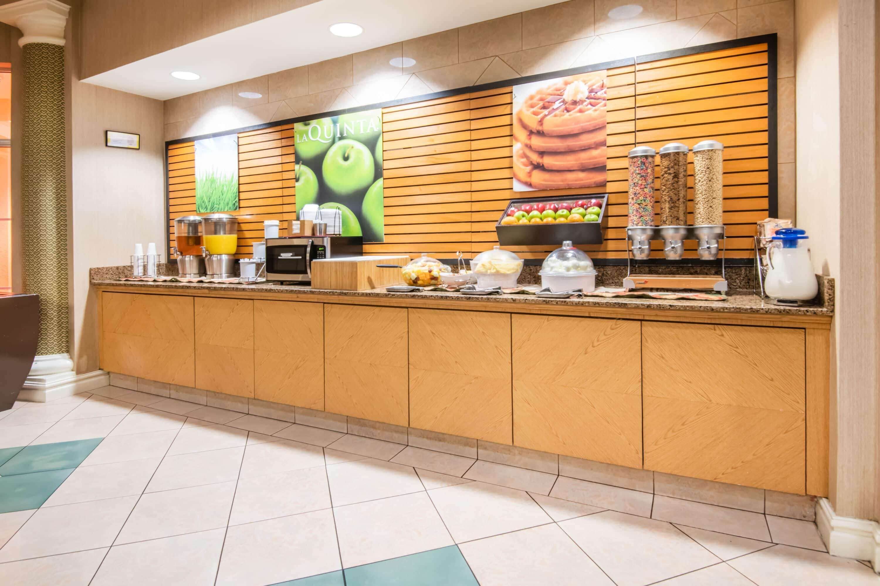 Un espace d’accueil d’hôtel avec un comptoir en bois, une machine à café et un présentoir de fruits.