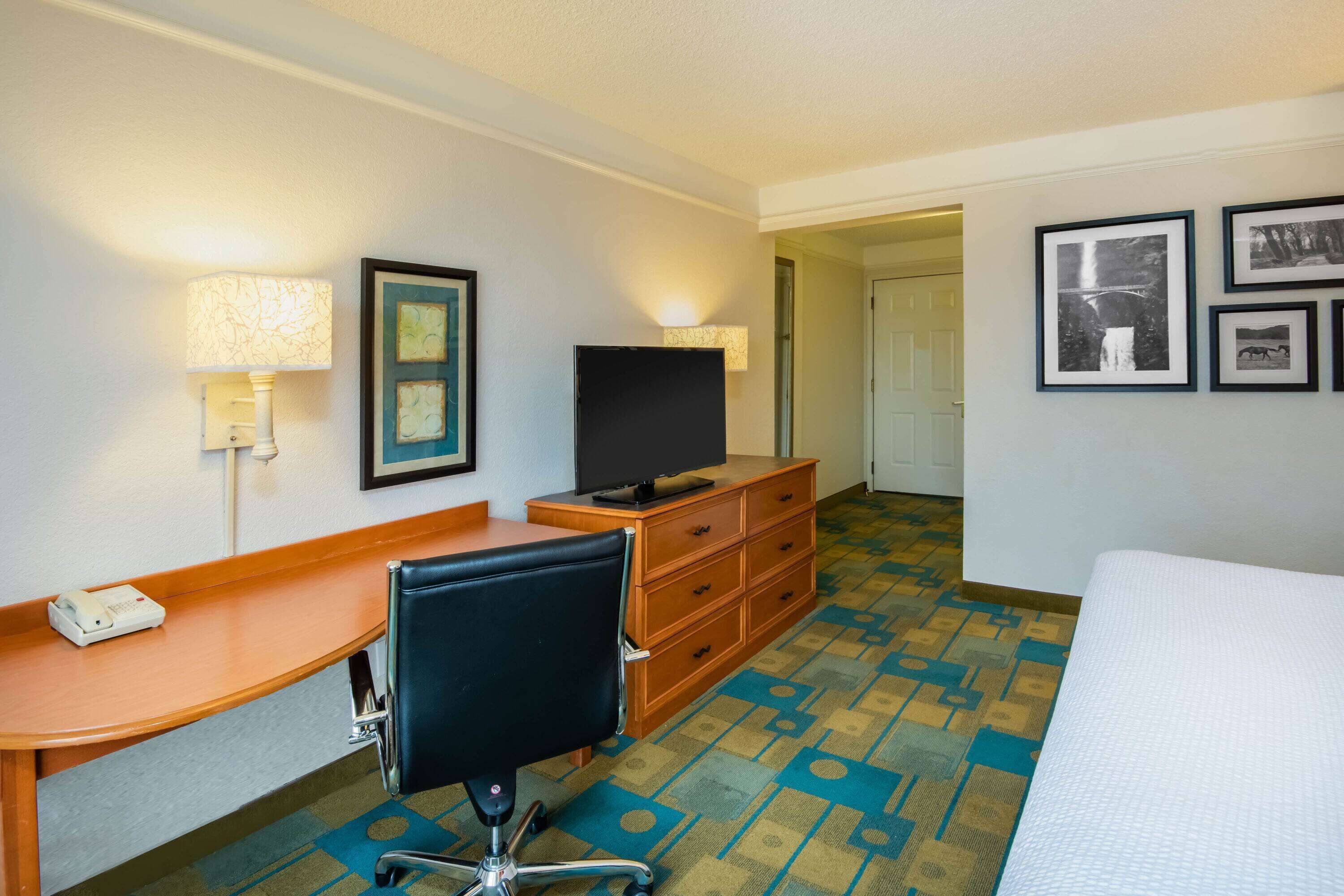 Een hotelkamer met een bureau, stoel, televisie, dressoir en bed.