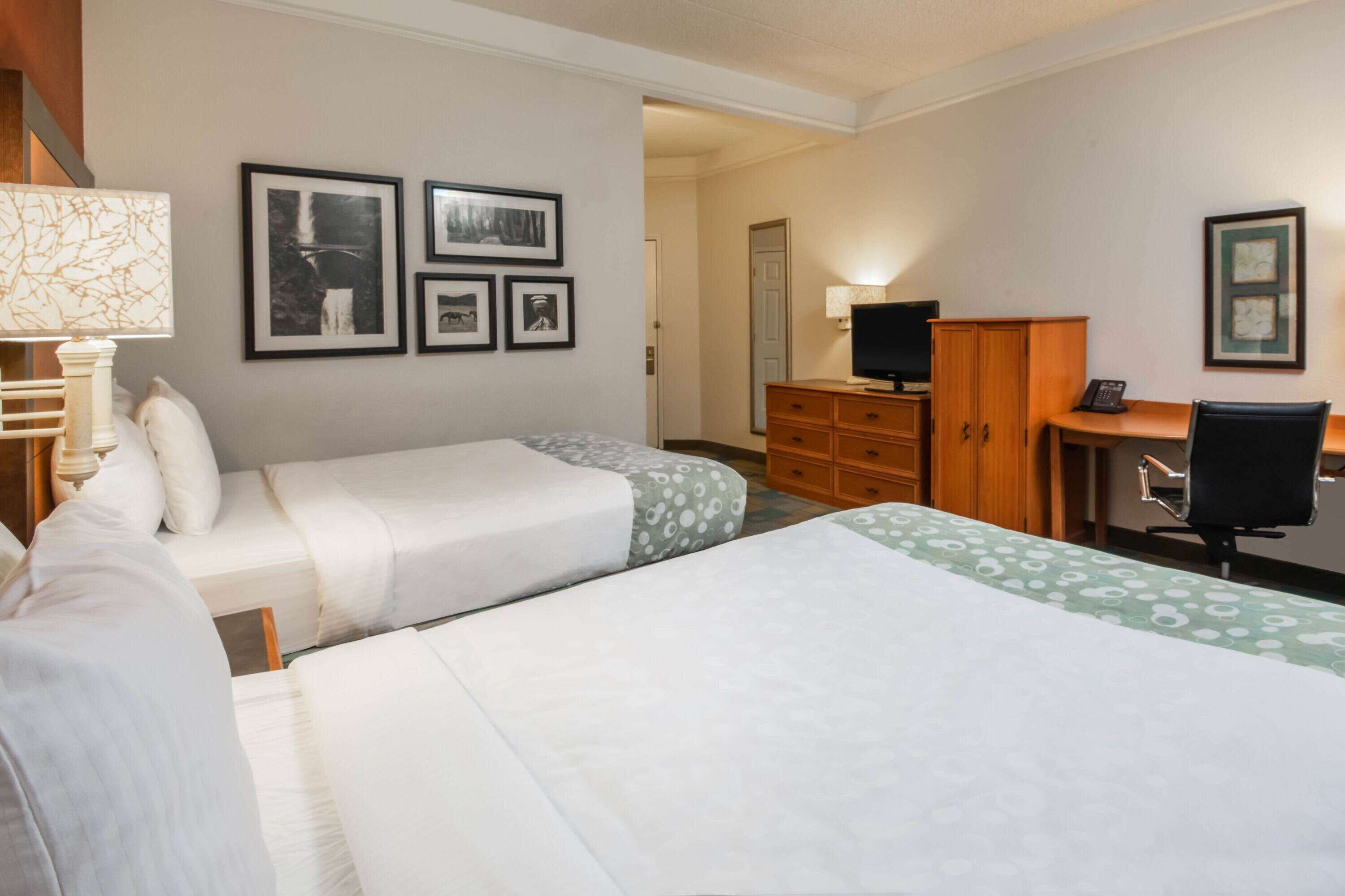A hotel room with two beds, a desk, a chair, a TV, and a dresser.