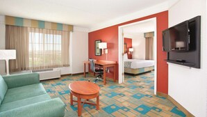 Quarto de hotel com um sofá verde, uma cadeira de madeira, uma mesa de escritório, uma televisão e uma cama.