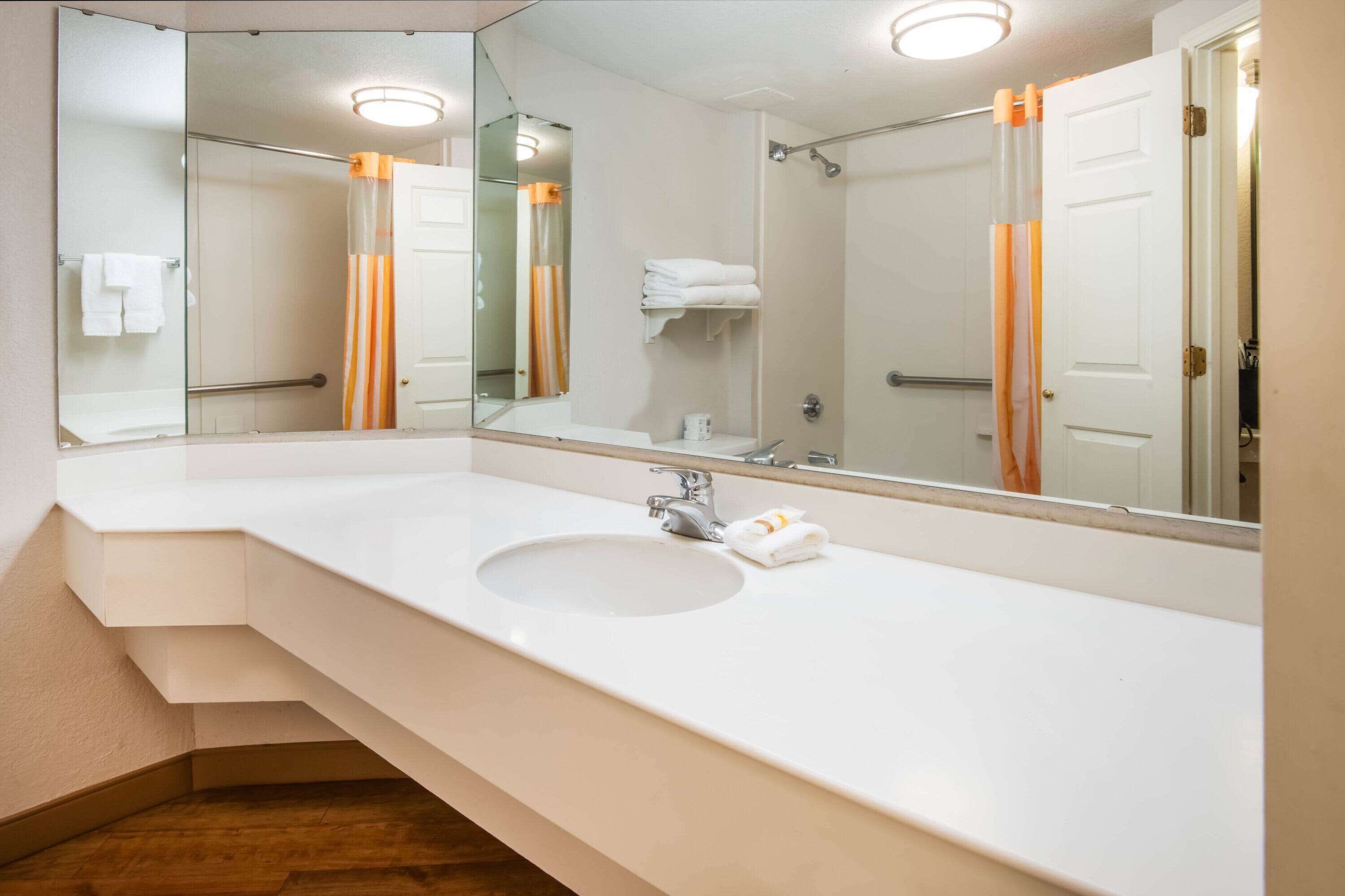 A modern bathroom with a large mirror, white sink, and a shower area.