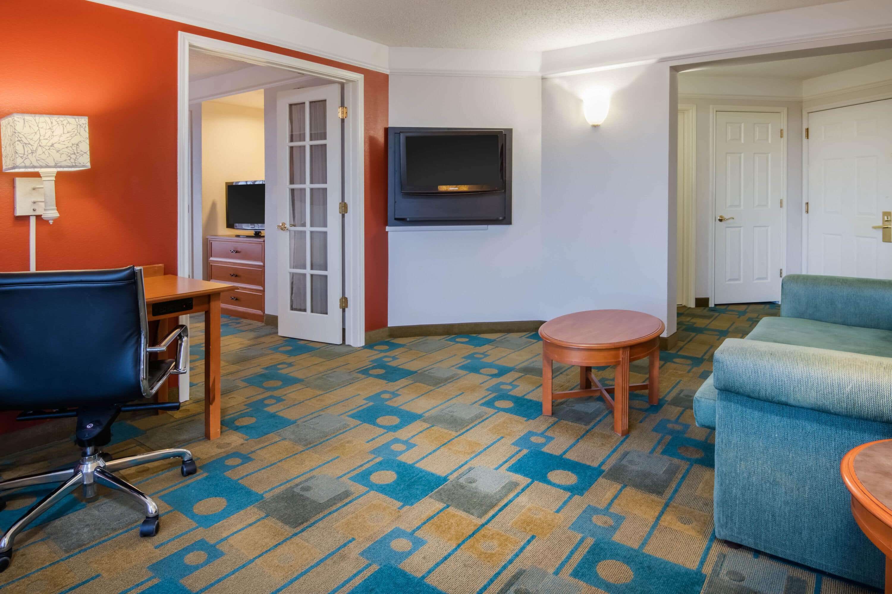 Una camera d'albergo con un letto, una scrivania, una sedia, una televisione e una moquette fantasia.