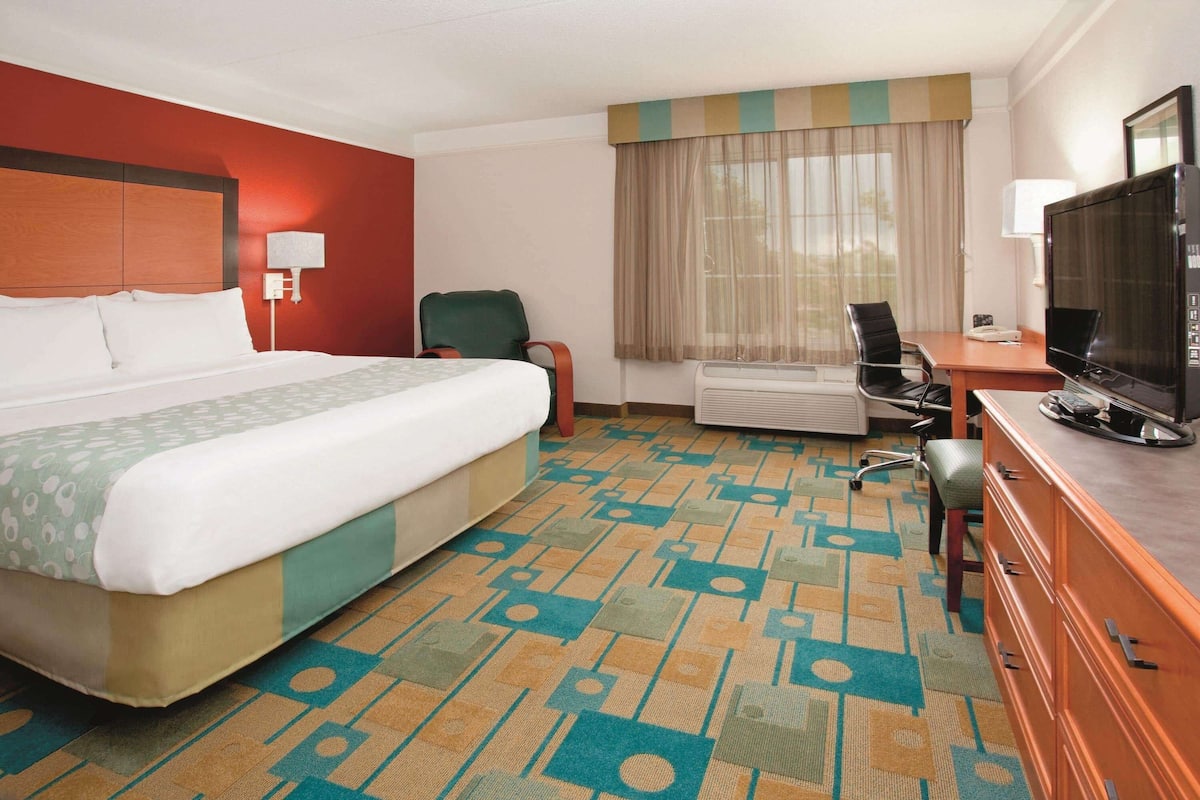 Een hotelkamer met een groot bed, een bureau met een televisie, een stoel en een raam met gordijnen.