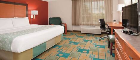 A hotel room with a large bed, a desk with a television, a chair, and a window with curtains.