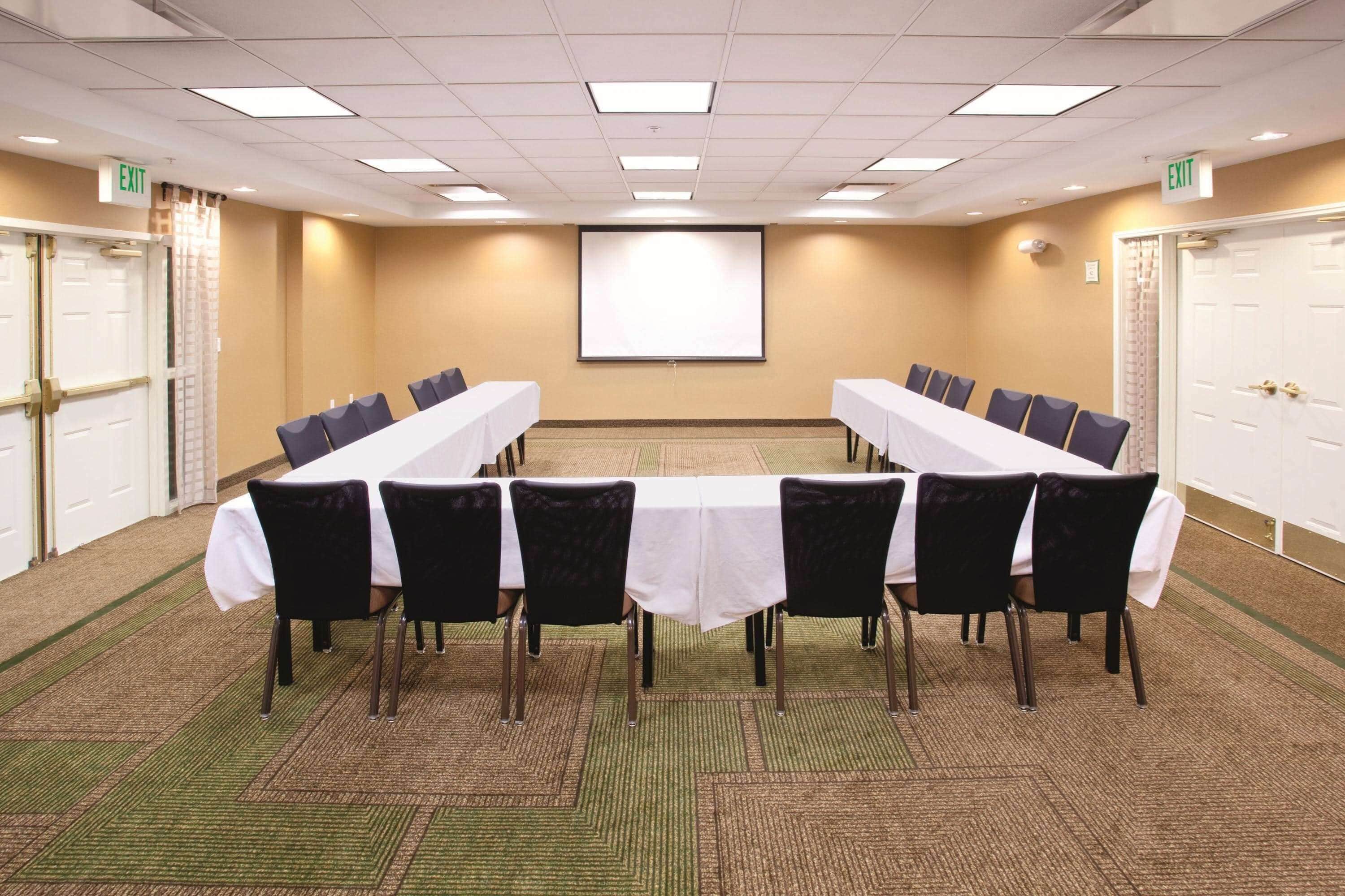 A conference room with a long table, chairs, a projector screen, and carpeted flooring.