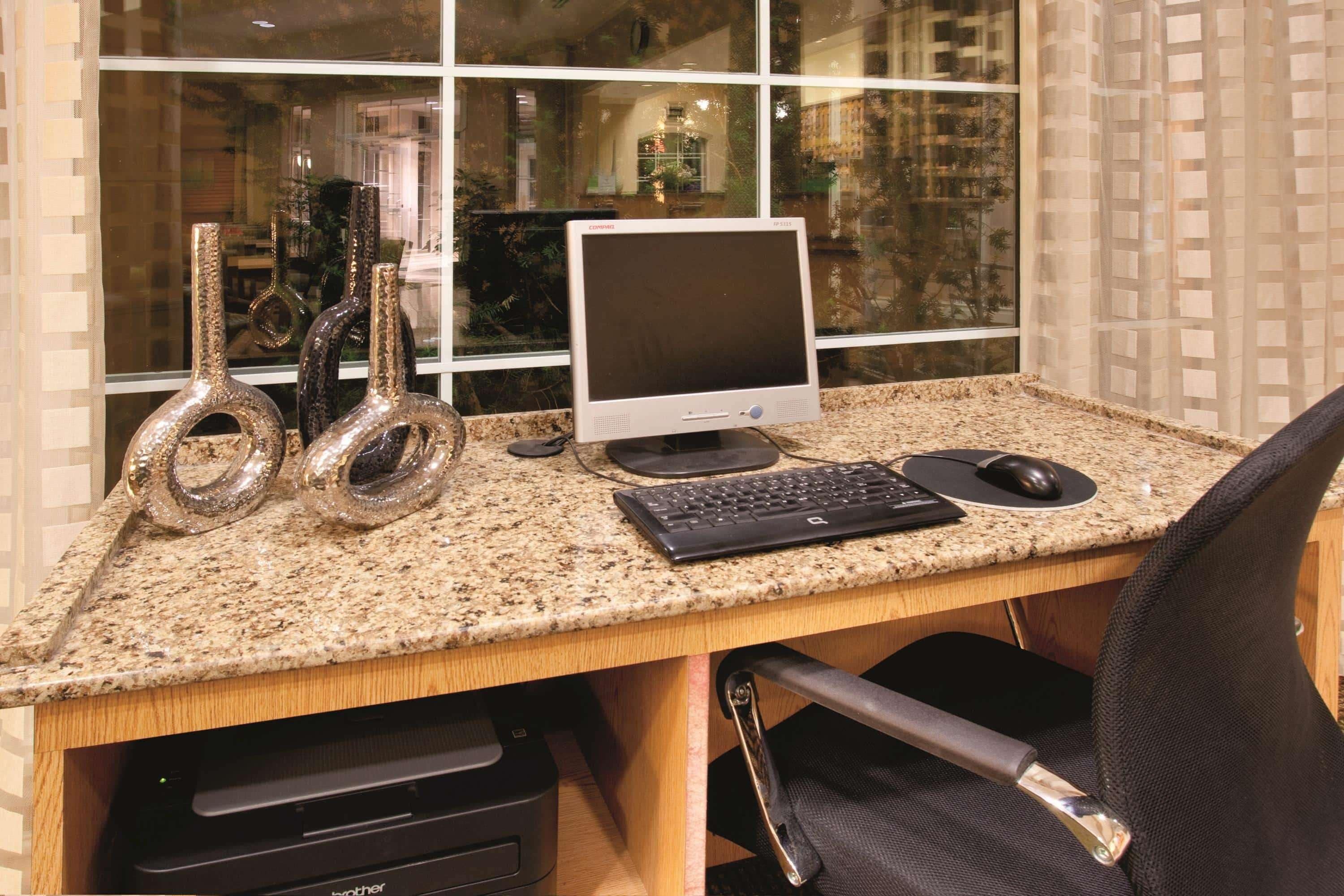 A computer desk with a desktop monitor, keyboard, mouse, and decorative glass vases.