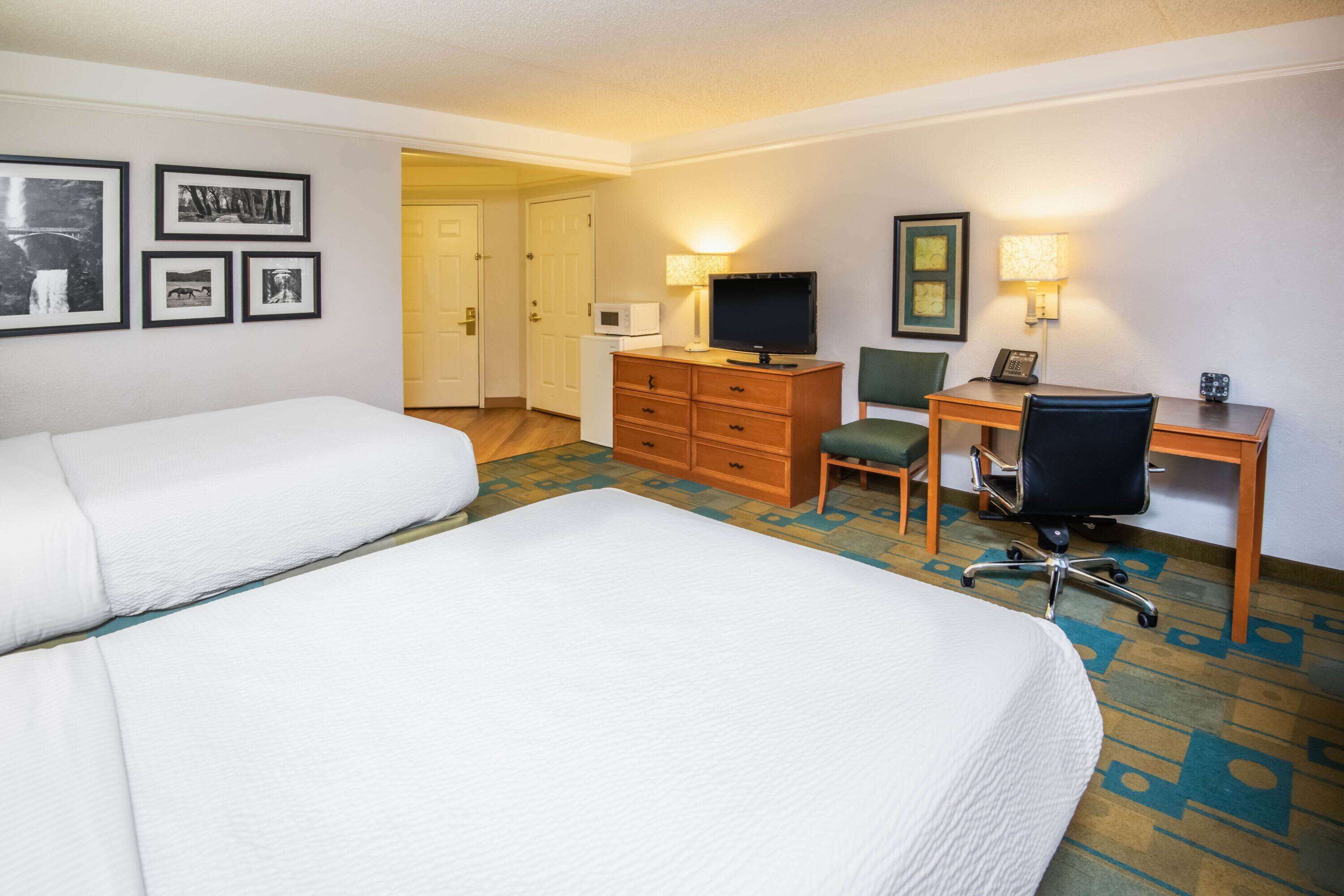 A hotel room with two beds, a desk with a computer, a chair, a dresser, and a television.