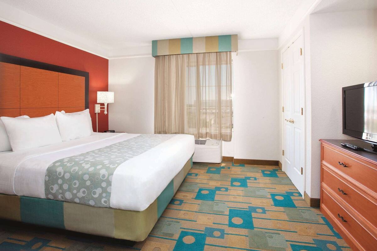 Een hotelkamer met een bed, een televisie, een dressoir en een raam met gordijnen.