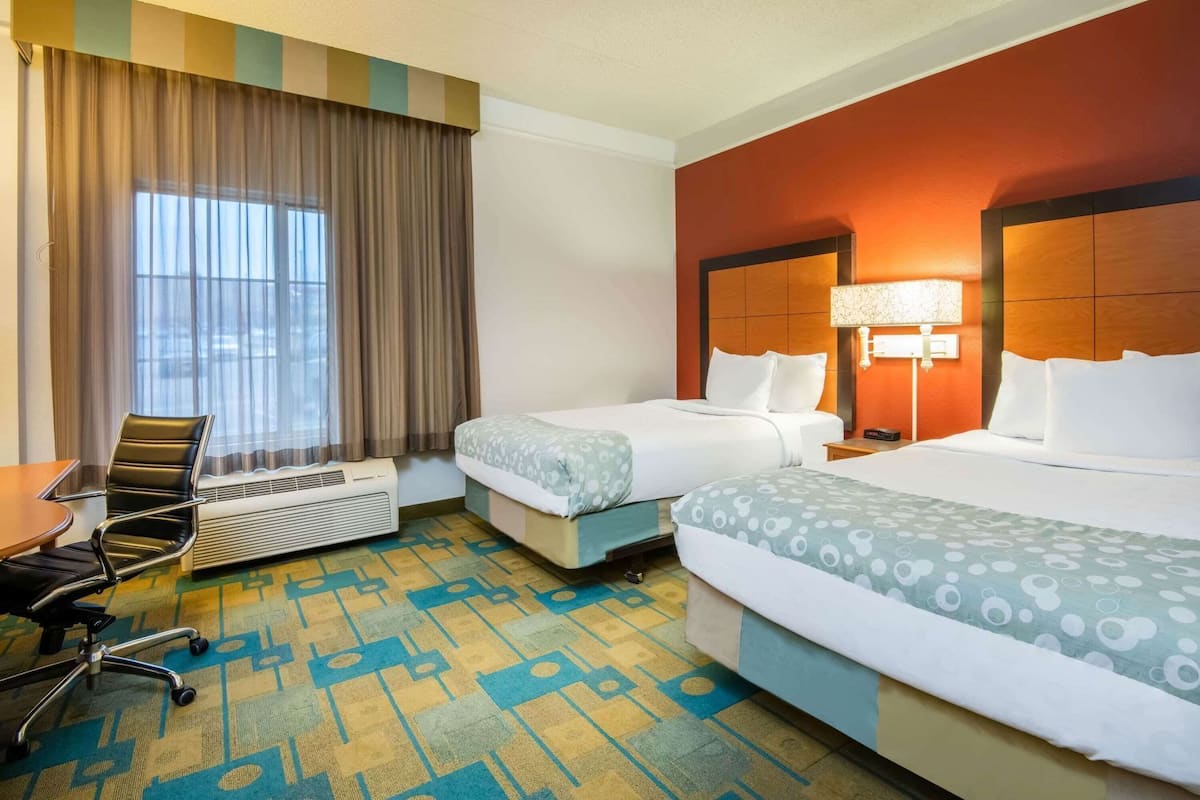 Een hotelkamer met twee bedden, een bureau, een stoel, een airconditioning en een raam met gordijnen.
