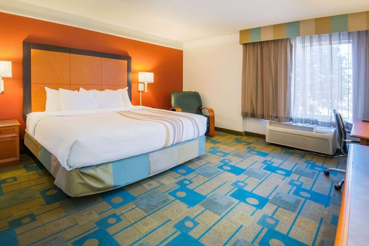 Een hotelkamer met een bed, een stoel, een bureau en een raam met gordijnen.