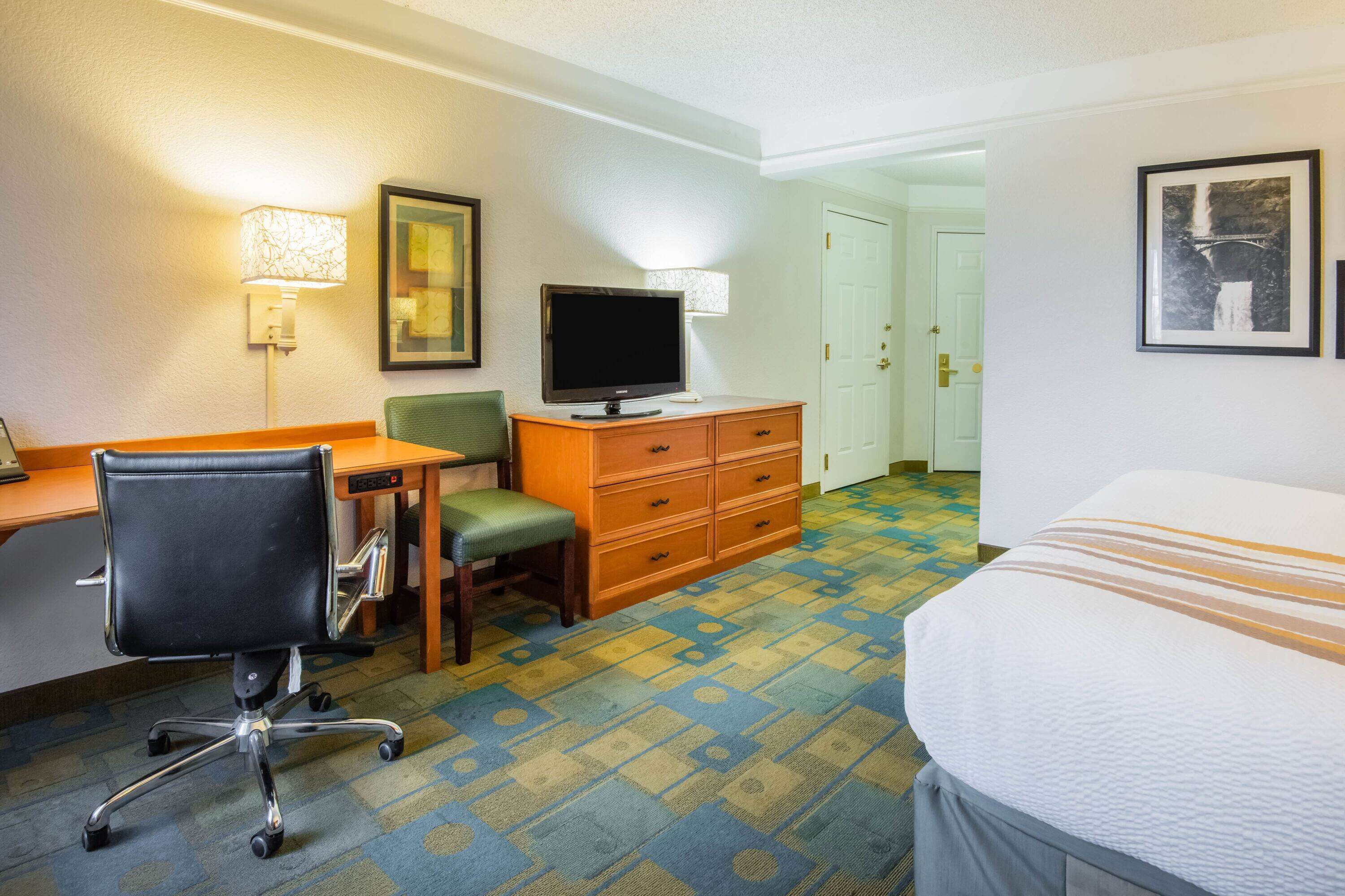 Une chambre d’hôtel comprenant un lit, un bureau, une chaise, une télévision, une commode et un sol recouvert de moquette.